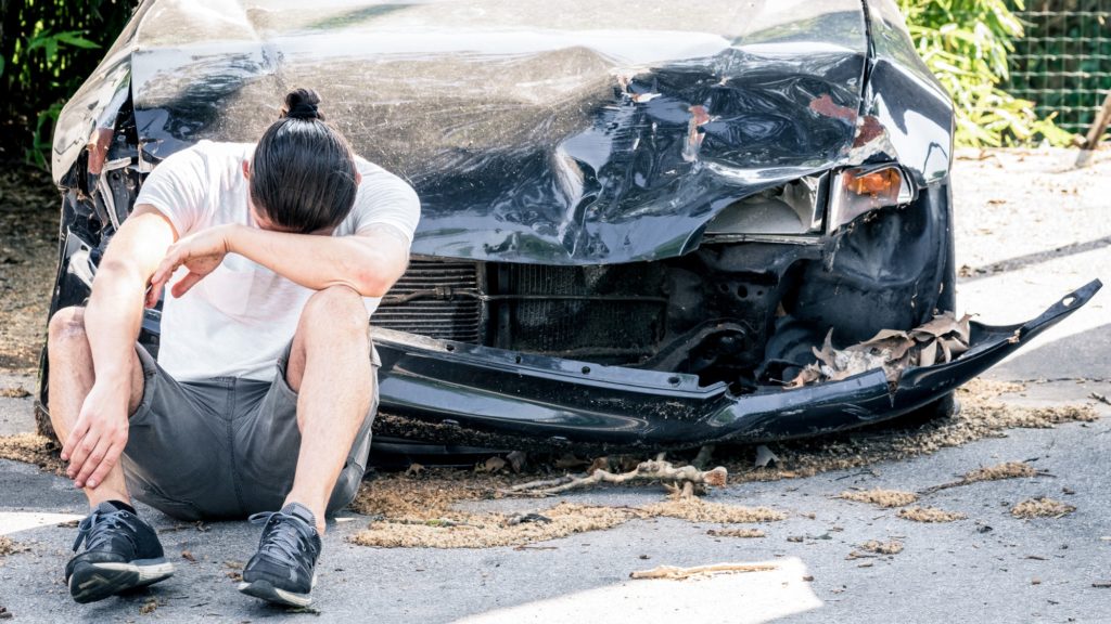 Man crying on his old damaged car after crash accident